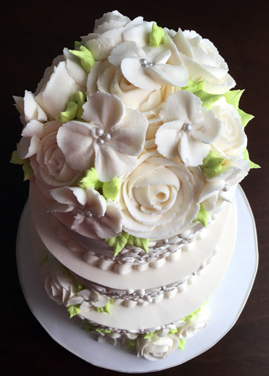 Top view of 3 tier buttercream wedding cake, decorated with cascading buttercream scrolls, sugar pearls, buttercream roses and small flowers