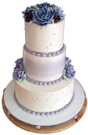 3 tier buttercream wedding cake with hi-lights of lilac butttercream; decorated with different shades of purple roses, silver ribbons, silver dragees and lilac snail trail borders