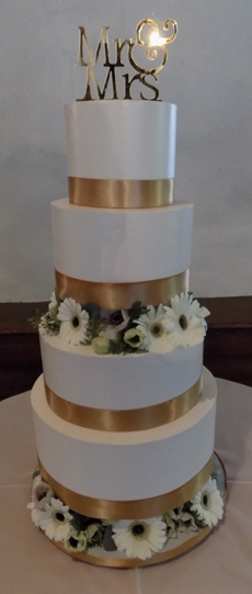 4 Tier buttercream seperator wedding cake, decorated with gold ribbons and an assortment of fresh white flowers. Wedding cake was delivered in Hallam PA.
