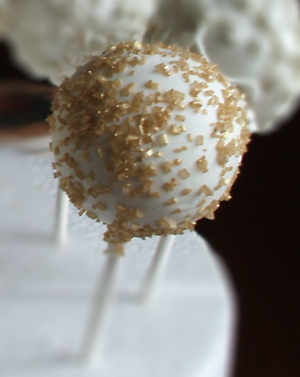 Chocolate raspberry cake pop dipped in white chocolate and decorated with gold sugar sprinkles