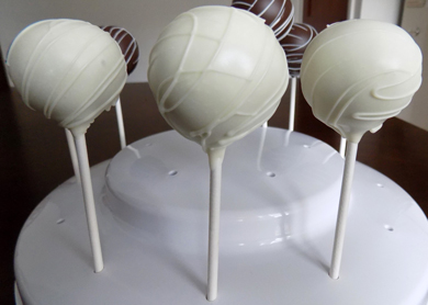 Yellow cake pops, dipped and white chocolate and decorated with white chocolate stripes