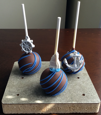 Nautical themed cake pops. Yellow cake pops, dipped in dark chocolate decorated with dark chocolate stripes and decorated with silver fondant anchors, sail boats and ship's wheels