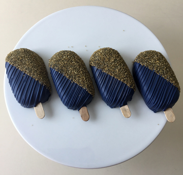 Navy blue chocolate dipped cakesickes, decorated with half decorated with chocolate stripes and the other half decorated with gold sanding sugar.