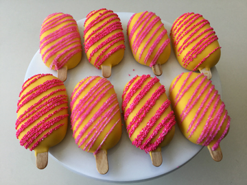 Yellow chocolate dipped cakesicles, decorated with pink and hot pink nonpareil stripes.