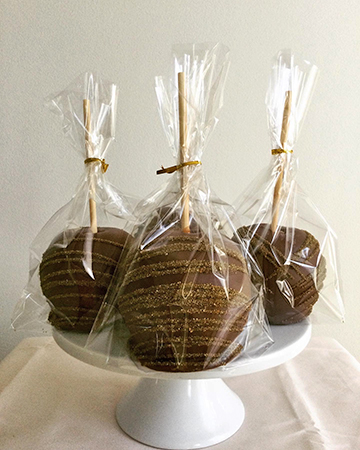 Caramel apples, dipped in milk chocolate and decorated with gold sanding sugar stripes placed in bags