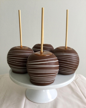 Caramel apples, dipped in milk chocolate and decorated with white chocolate stripes