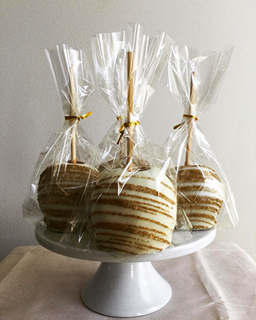 Caramel apples, dipped in white chocolate and decorated with gold sanding sugar stripes placed in bags