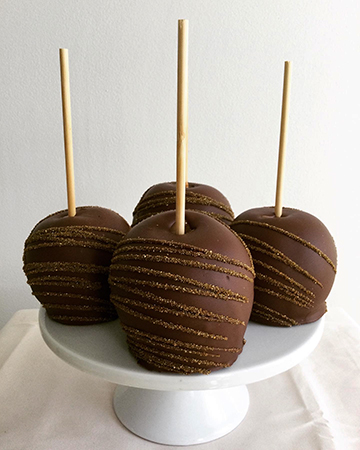 Caramel apples, dipped in milk chocolate and decorated with gold sanding sugar stripes