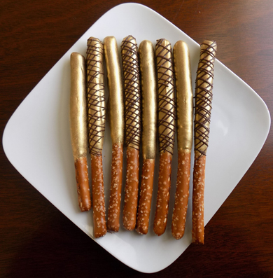 Tall pretzels sticks dipped in dark chocolate, painted gold and decorated with dark chocolate stripes
