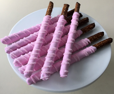 Tall pretzels dipped in light pink chocolate with sugar crystal stripes