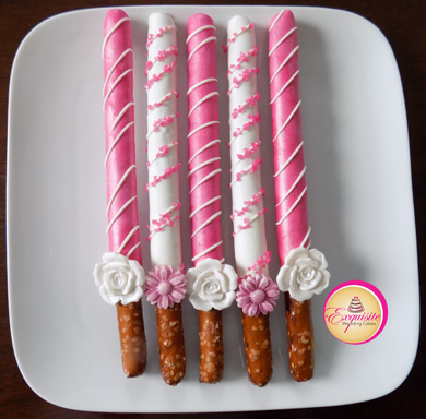 Tall pretzels rods dipped in pink and white chocolate, decorated with chocolate stripes, sugar crystals and edible sugar flowers