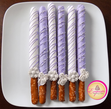 Tall pretzels rods dipped in white and lilac chocolate, decorated with chocolate stripes, silver sugar crystals and sugar flowers