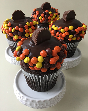 Chocolate cupcakes, filled with ganache, topped with peanut buttercream, dipped in ganache, with edges covered in mini Reese's pieces and topped with mini peanut butter cups
