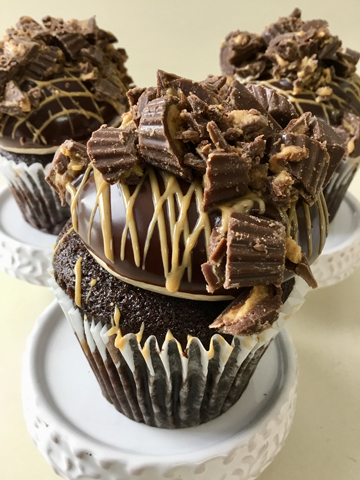 Chocolate cupcakes, filled with ganache, topped with peanut buttercream, dipped in ganache, drizzled with peanut sauce and topped with pieces of peanut butter cups
