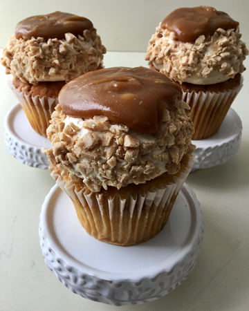 Vanilla toffee bits cupcakes, topped with vanilla buttercream, with sides covered in homemade toffee bits and topped with thick caramel sauce