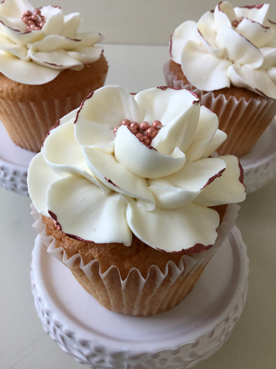 Wedding cupcakes decorated with large white buttercream flowers with rose gold pearl centers and rose gold edges