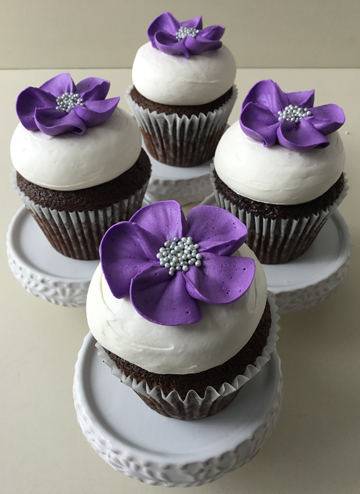 Chocolate cupcakes, topped with vanilla buttercream and decorated with light purple buttercream flowers with silver nonpareil centers