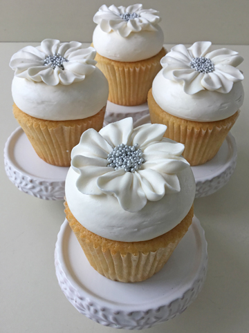 Vanilla cupcakes, topped with vanilla buttercream and decorated with white buttercream flowers with silver nonpareils