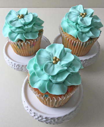 Confetti cupcakes decorated with light teal buttercream flowers with gold pearl centers