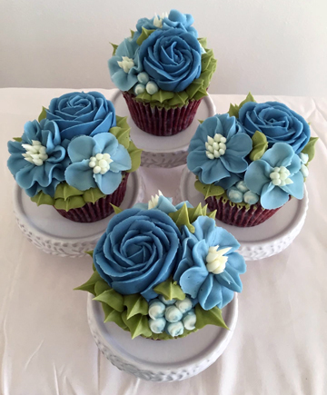 Red velvet cupcakes decorated with ombre blue buttercream roses, blossom flowers and leaves