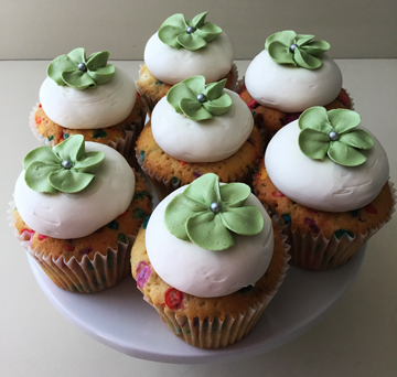 Confetti cupcakes, topped with vanilla buttercream and decorated with sage buttercream blossom flowers, with silver pearl centers