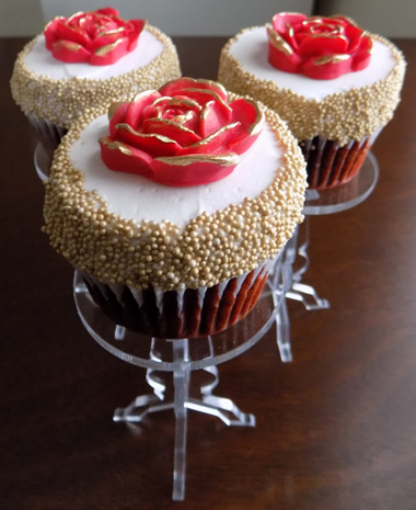 Red velvet cupcakes, filled with cream cheese icing, iced with vanilla buttercream and decorated with gold non-perils and red fondant roses with the edges painted in gold